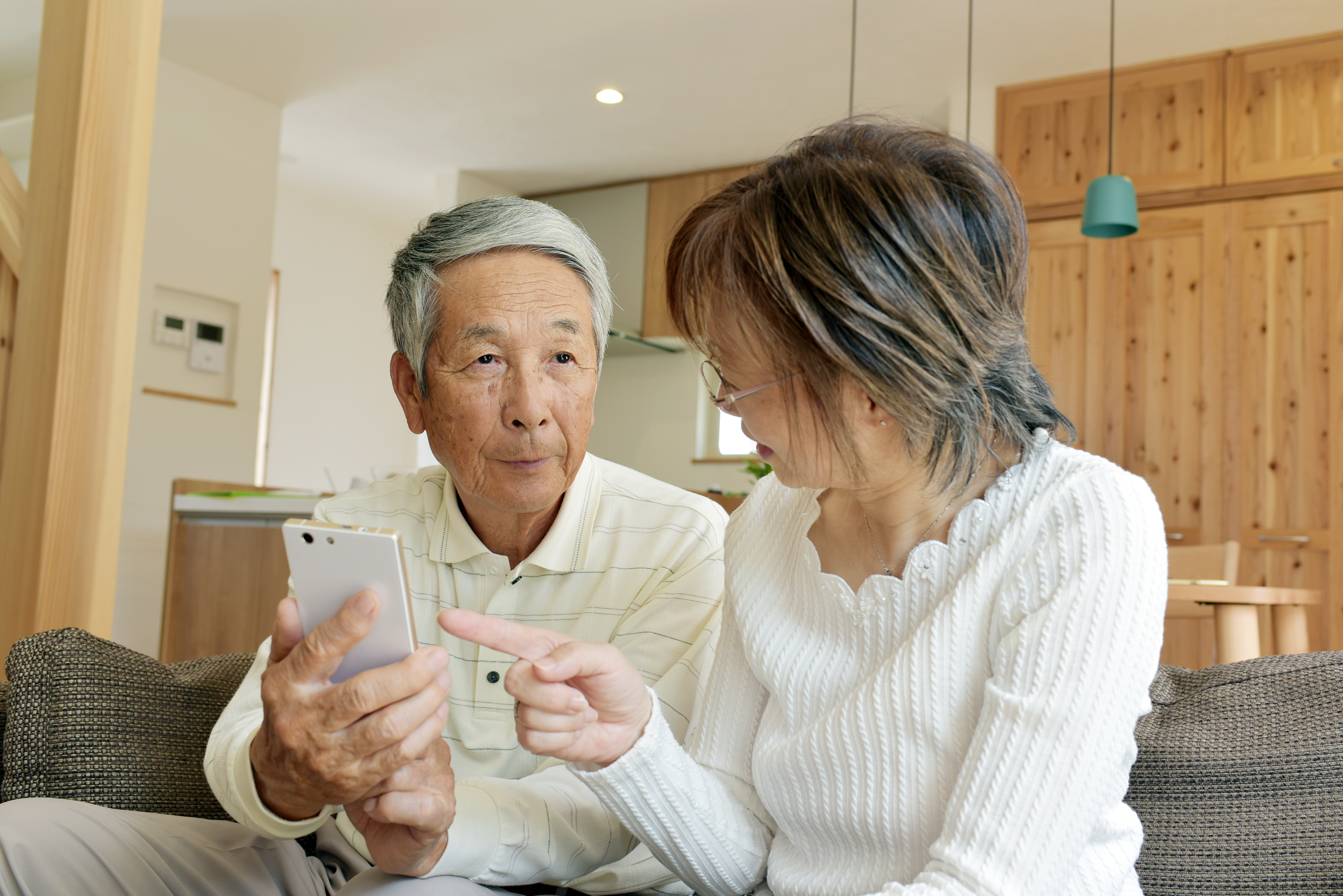 リビングのソファでスマホを眺めるシニア夫婦